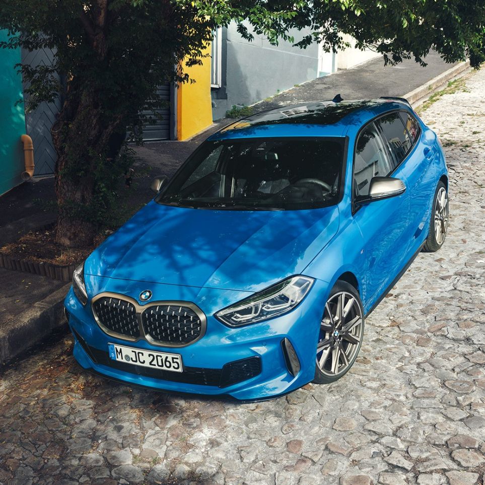 BMW serije 1 sa strane ceste. BMW serije 1 u Misano Blue metalik boji, tročevrtinski prikaz prednjeg kraja, prikaz modela parkiranog sa strane ceste iz ptičje perspektive.