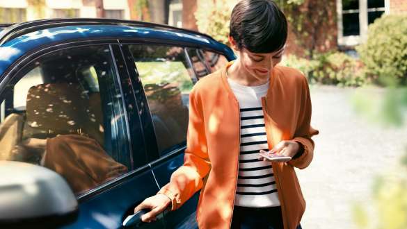 Žena gleda na pametni telefon i otvara vrata svog BMW-a BMW Teleservices žena gleda na pametni telefon i otvara vrata svog BMW-a