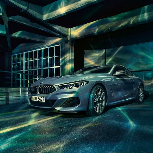 BMW M850i xDrive Coupé, tročetvrtinski prednji pogled. BMW M850i xDrive Coupé u Barcelona Blue metalik, tročetvrtinski prednji pogled ispred građevine.