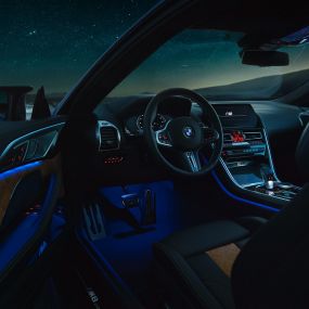 Unutrašnjost BMW M8 Competition Coupé. BMW M8 Competition Coupé, unutrašnjost po noći sa M kožnim upravljačem i plavim ambijentalnim svjetlom sa otvorenim vratima vozača.