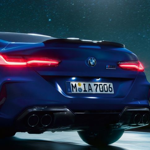 M difuzer u Carbon Black boji. BMW M8 Competition Coupé u Marina Bay Blue metalik, krupni plan straga po noći sa M difuzer u Carbon Black boji.