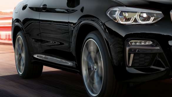 BMW X4 M40i i BMW X4 M40d, tročetvrtinski bočni prikaz. BMW X4 M40i i BMW X4 M40d u Black Sapphire metalik boji, u vožnji, vanjština, tročetvrtinski bočni prikaz s rotirajućim lakometalnim kotačem.