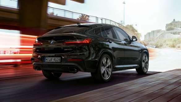 BMW X4 M40i i BMW X4 M40d, tročetvrtinski stražnji prikaz. BMW X4 M40i i BMW X4 M40d u Black Sapphire metalik boji, u vožnji, vanjština, tročetvrtinski stražnji prikaz sa svijetlosnim trakama.