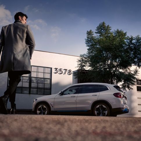 BMW iX3 G08 bočni prikaz ispred zgrade s muškarcem BMW iX3 G08 2020 Mineral White metalik bočni prikaz ispred zgrade s muškarcem