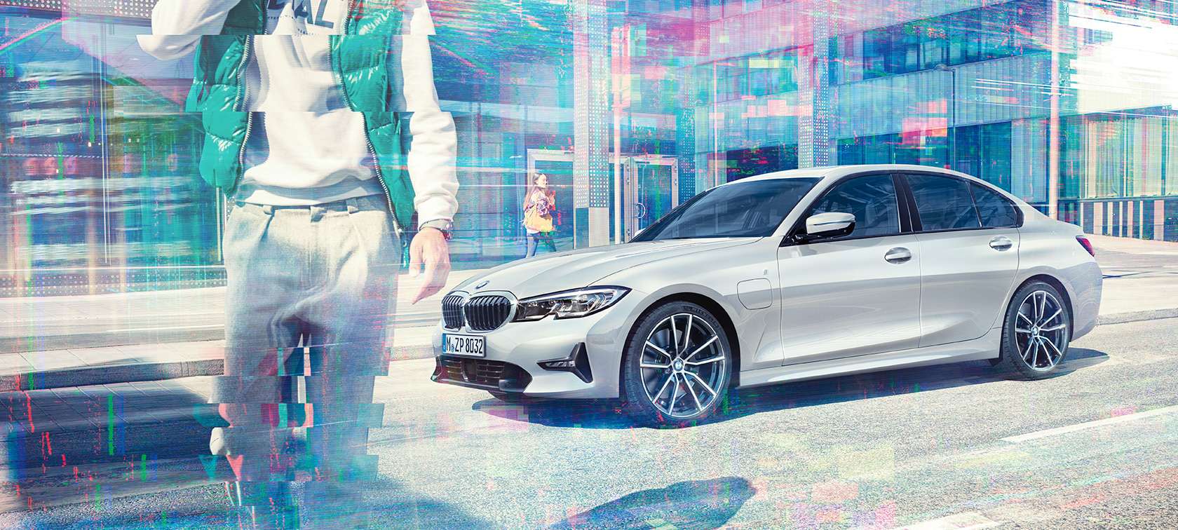 BMW serije 3 limuzina, bočni prikaz BMW-a 330e. Tročetvrtinski bočni prikaz BMW-a 330e limuzina ispred urbane staklene zgrade s prolaznicima koji hodaju.
