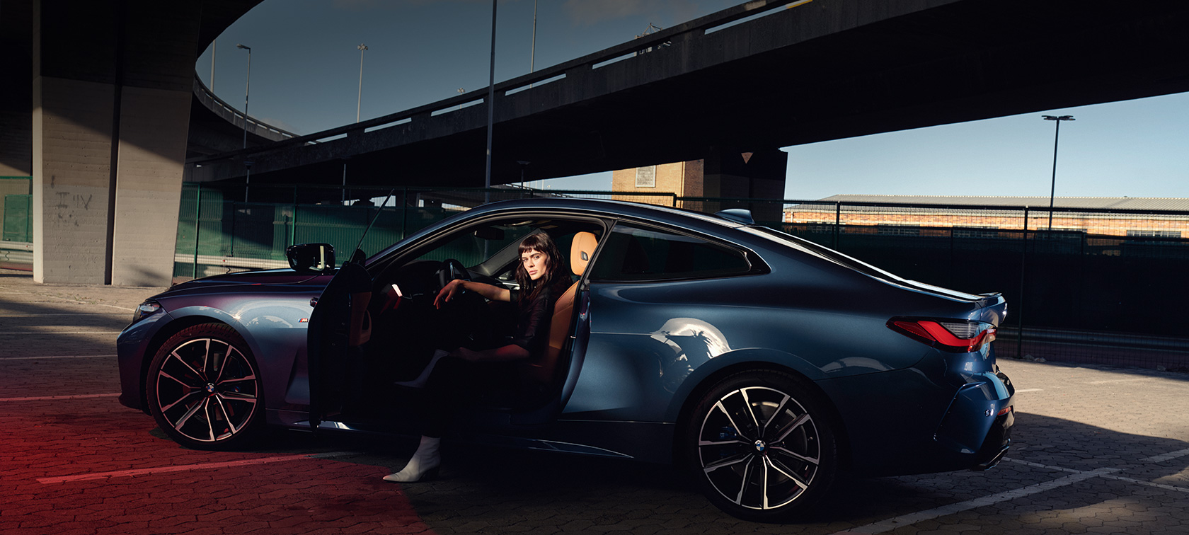 Tročetvrtinski pogled straga BMW serije 4 Coupé G22 2020 BMW serije 4 Coupé G22 2020 Arctic Race Blue metalik tročetvrtinski pogled na stražnja svjetla sa modelom koji stoji pokraj vozila