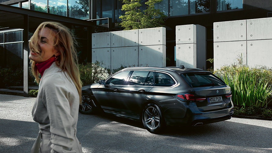 Žena ispred BMW serije 5 Touringa G31 Facelift 2020 u Sophisto grey metalik Žena ispred parkiranog BMW serije 5 Touring G31 Facelift 2020 u Sophisto grey metalik