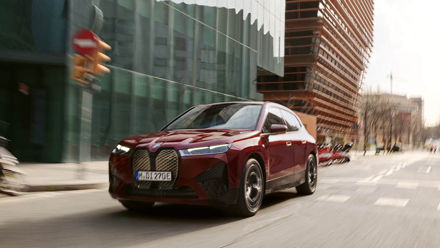 BMW iX i20 2021 električni SUV; Pomoć u vožnji BMW-a iX xDrive50 BMW iX i20 2021 električni SUV; BMW iX xDrive50 Aventurin Red boje u vožnji u urbanoj okolini
