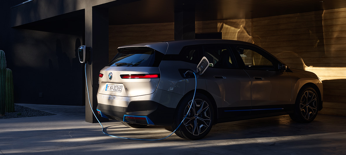 BMW iX tročetvrtinski pogled straga za vrijeme punjenja na BMW Wallbox BMW iX Cashmere Silver i20 tročetvrtinski pogled straga za vrijeme punjenja na BMW Wallbox