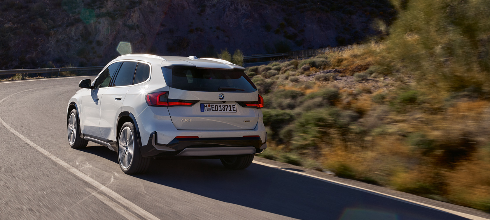 BMW iX1 U11 BEV vozna dinamika značajke video BMW iX1 U11 BEV 2022 Mineral White metalik dvotrećinski pogled straga planinska cesta u vožnji vozna dinamika značajke video