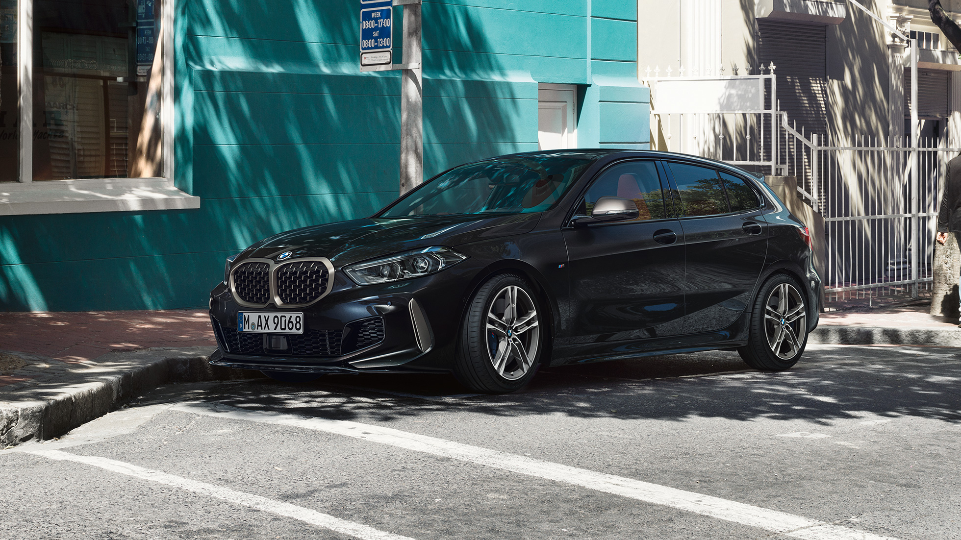 BMW M135i xDrive, tročetvrtinksi bočni prikaz. Potpuno novi BMW M135i xDrive u Black Sapphire metalik boji, tročetvrtinksi bočni prikaz prilikom parkiranja.