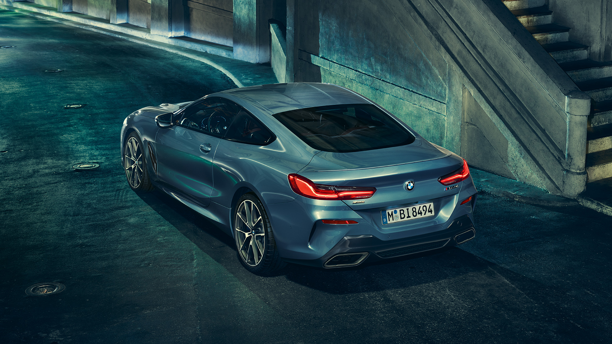 BMW M850i xDrive Coupé, tročetvrtinski stražnji lijevi pogled. BMW M850i xDrive Coupé u Barcelona Blue metalik, tročetvrtinski stražnji lijevi pogled, u mirovanju po noći.