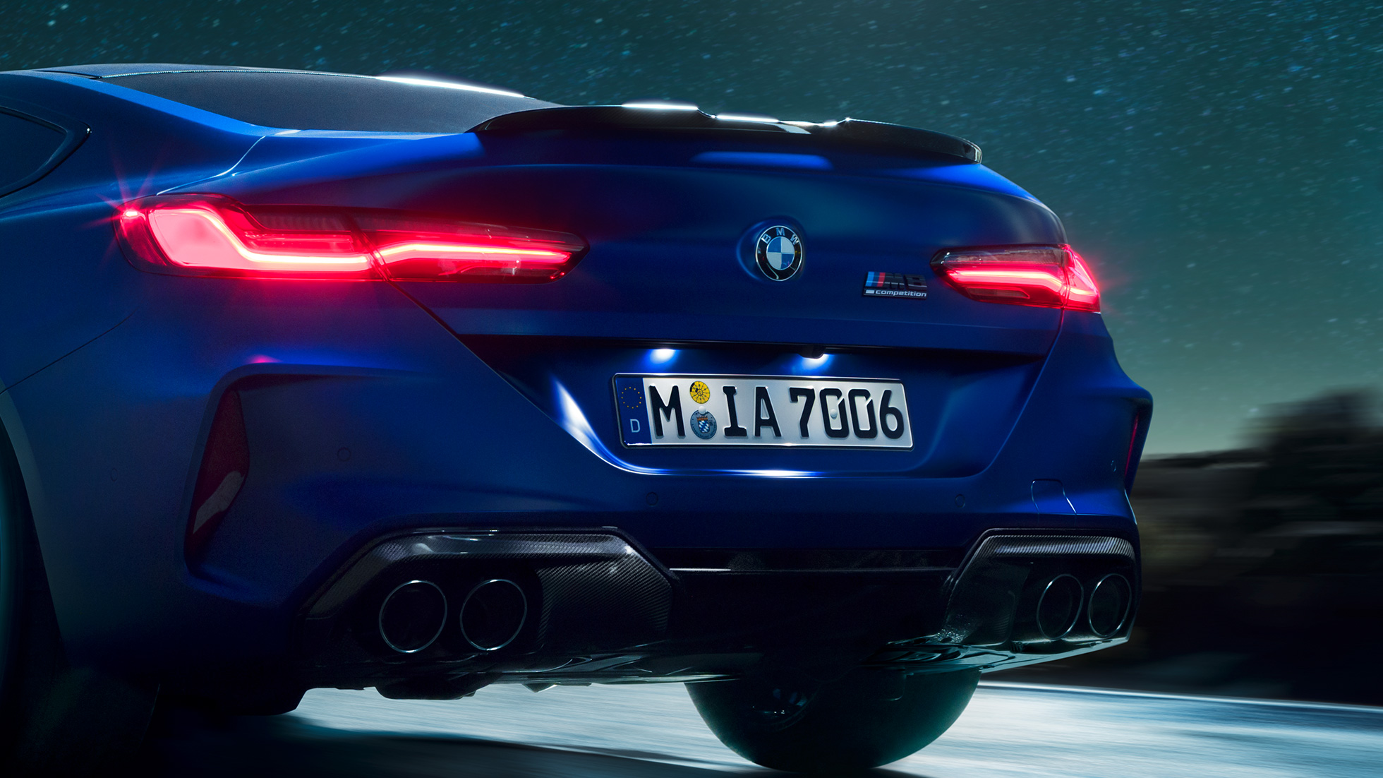 M difuzer u Carbon Black boji. BMW M8 Competition Coupé u Marina Bay Blue metalik, krupni plan straga po noći sa M difuzer u Carbon Black boji.