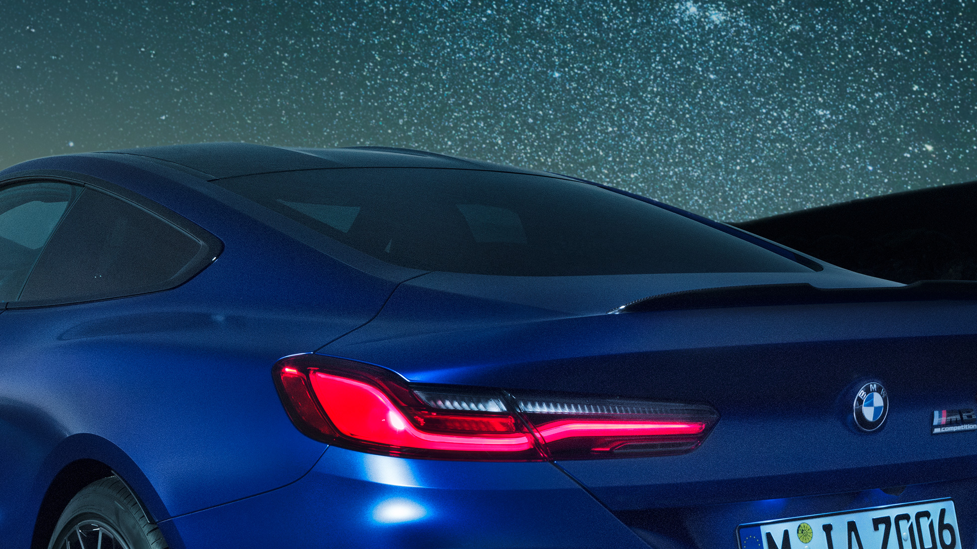 M stražnji spojler BMW M8 Competition Coupé u Marina Bay Blue metalik, krupni plan po noći bočnog dijela sa M stražnjim spojlerom u karbonu.