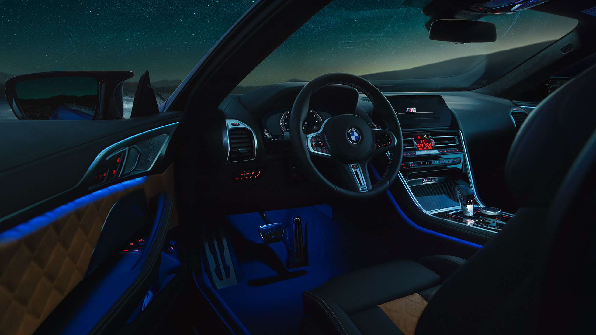 Unutrašnjost BMW M8 Competition Coupé. BMW M8 Competition Coupé, unutrašnjost po noći sa M kožnim upravljačem i plavim ambijentalnim svjetlom sa otvorenim vratima vozača.
