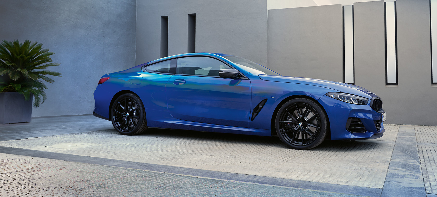 Pogled s boka BMW M850i xDrive Coupé G15 LCI Facelift 2022 BMW M850i xDrive Coupé G15 LCI Facelift 2022 M Portimao Blue metalik pogled s boka u mirovanju ispred zgrade