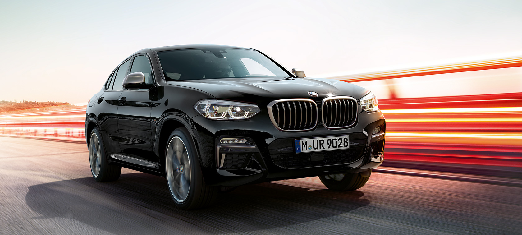 BMW X4 M40i i BMW X4 M40d, tročetvrtinski prednji prikaz, lijeva strana. BMW X4 M40i i BMW X4 M40d u Black Sapphire metalik boji, vanjština, tročetvrtinski prednji prikaz, lijeva strana sa svijetlosnim trakama.
