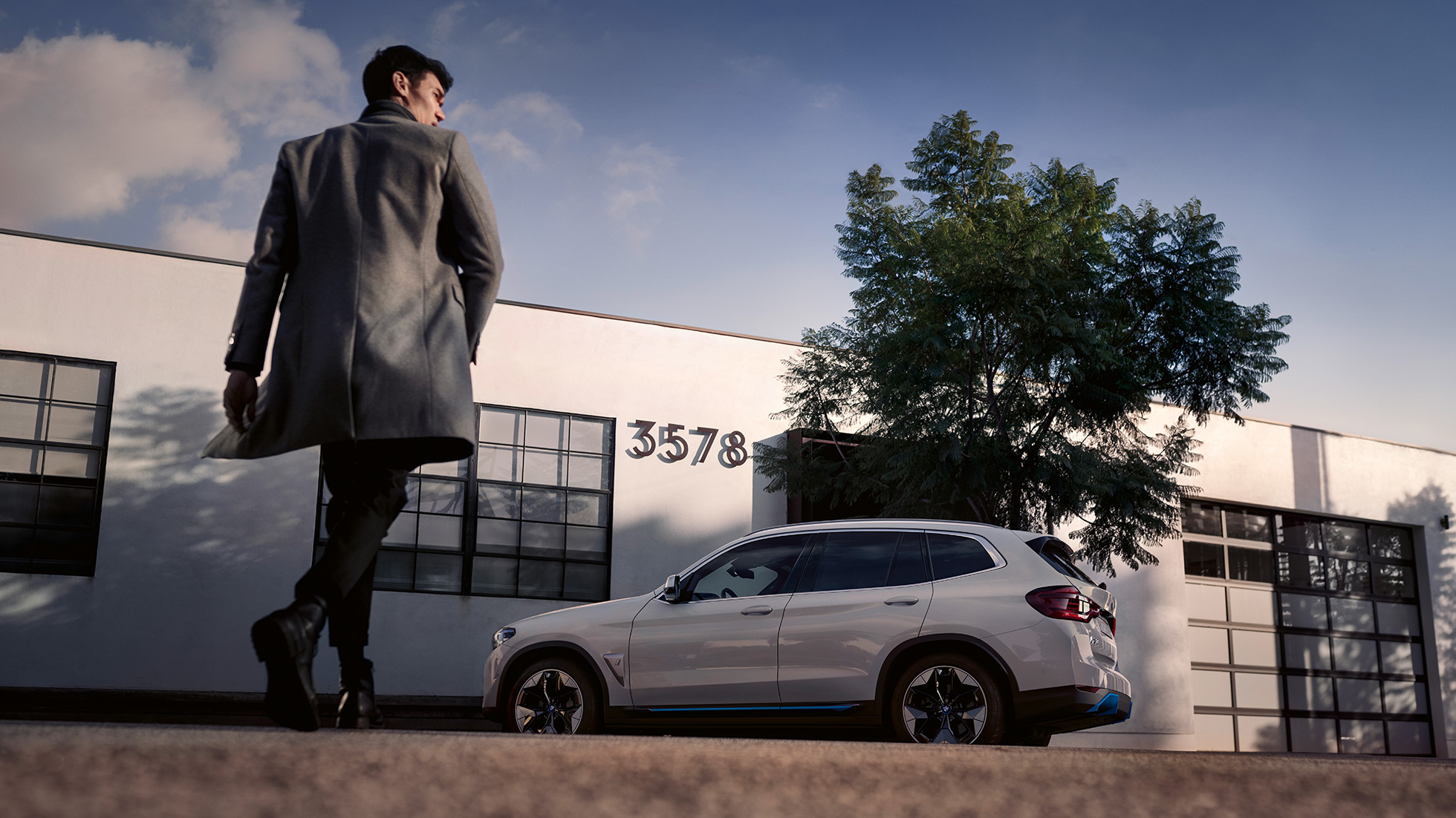 BMW iX3 G08 bočni prikaz ispred zgrade s muškarcem BMW iX3 G08 2020 Mineral White metalik bočni prikaz ispred zgrade s muškarcem