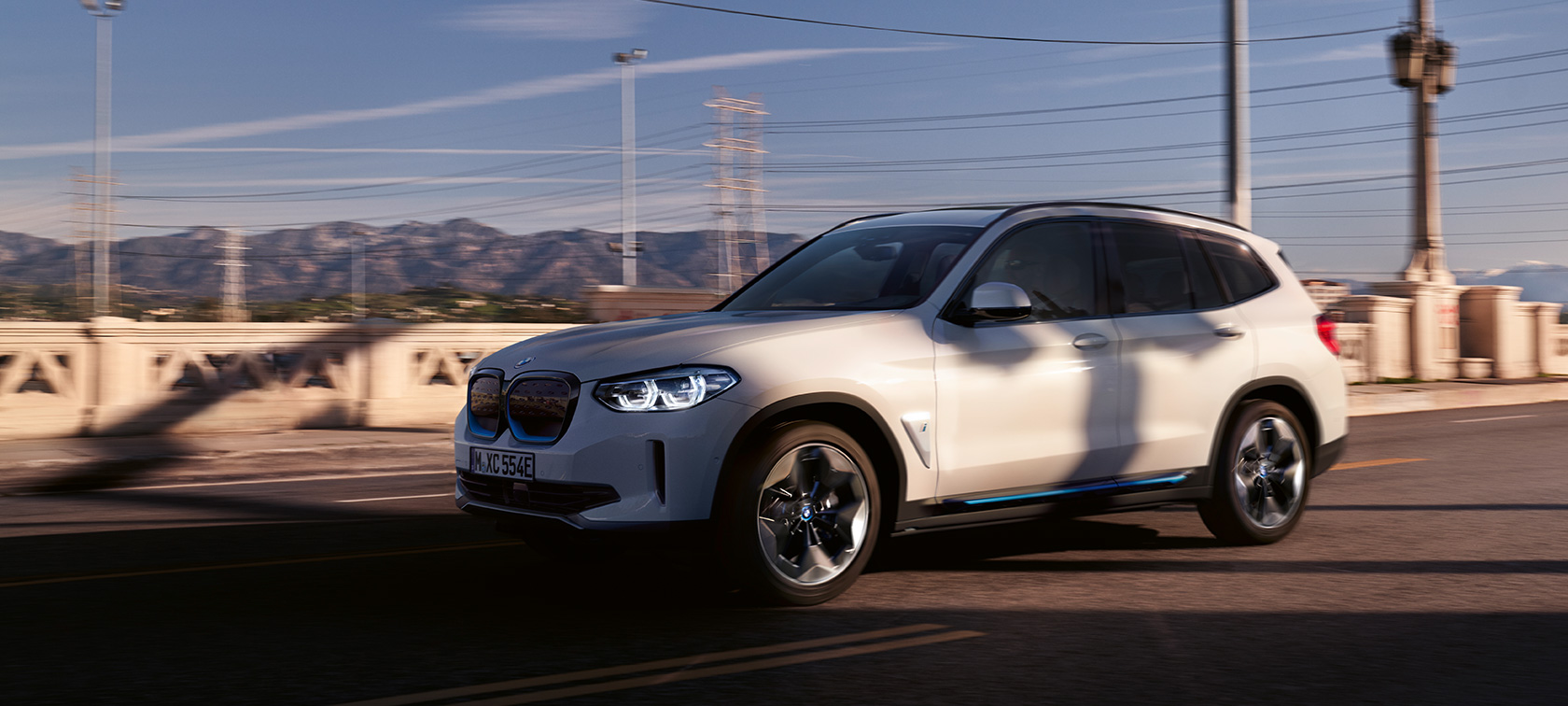 BMW iX3 G08 tročetvrtinski prednji prikaz na cesti BMW iX3 G08 2020 Mineral White metalik tročetvrtinski prednji prikaz u vožnji na cesti