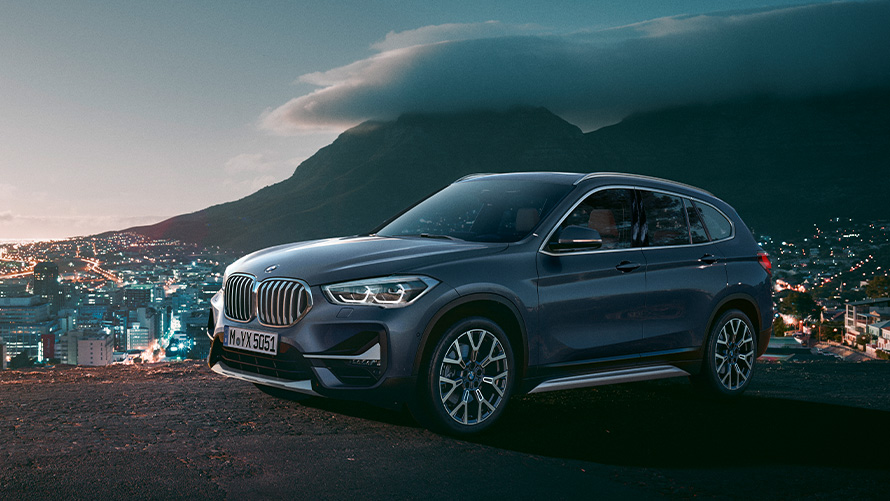 Tročetvrtinski bočni prikaz BMW-a X1 F48 druge generacije ispred grada BMW serija X; Tročetvrtinski bočni prikaz BMW-a X1 F48 druge generacije ispred grada