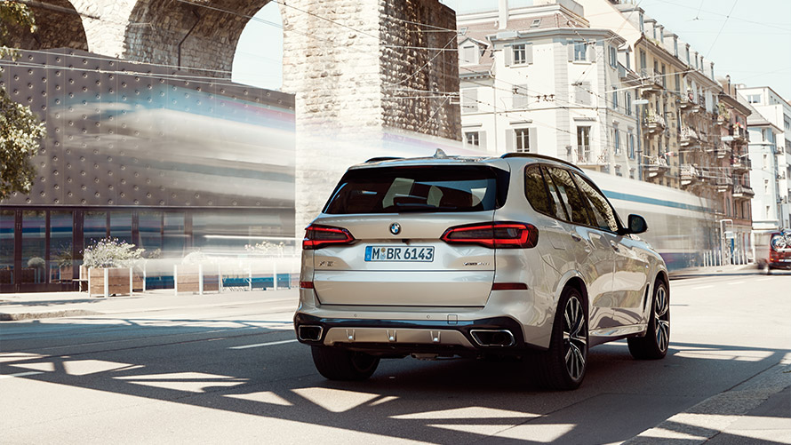 Tročetvrtinski prikaz stražnjeg kraja BMW-a X5 G05 četvrte generacije ispred zgrade BMW serije X; Tročetvrtinski prikaz stražnjeg kraja BMW-a X5 G05 četvrte generacije ispred zgrade