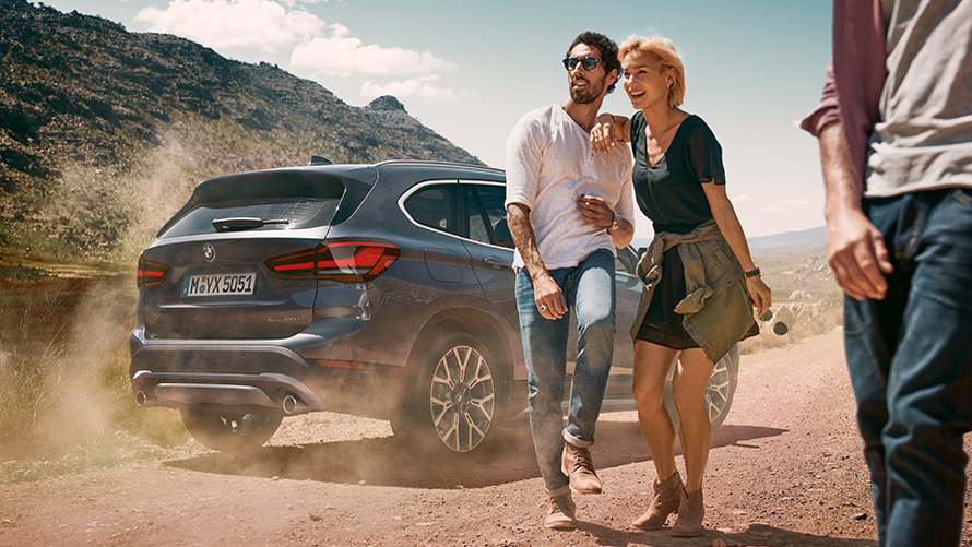 BMW X1 F48 LCI Storm Bay tročetvrtinski pogled straga BMW X1 F48 LCI Storm Bay tročetvrtinski pogled straga u mirovanju ispred krajolika sa ljudima u prvom planu