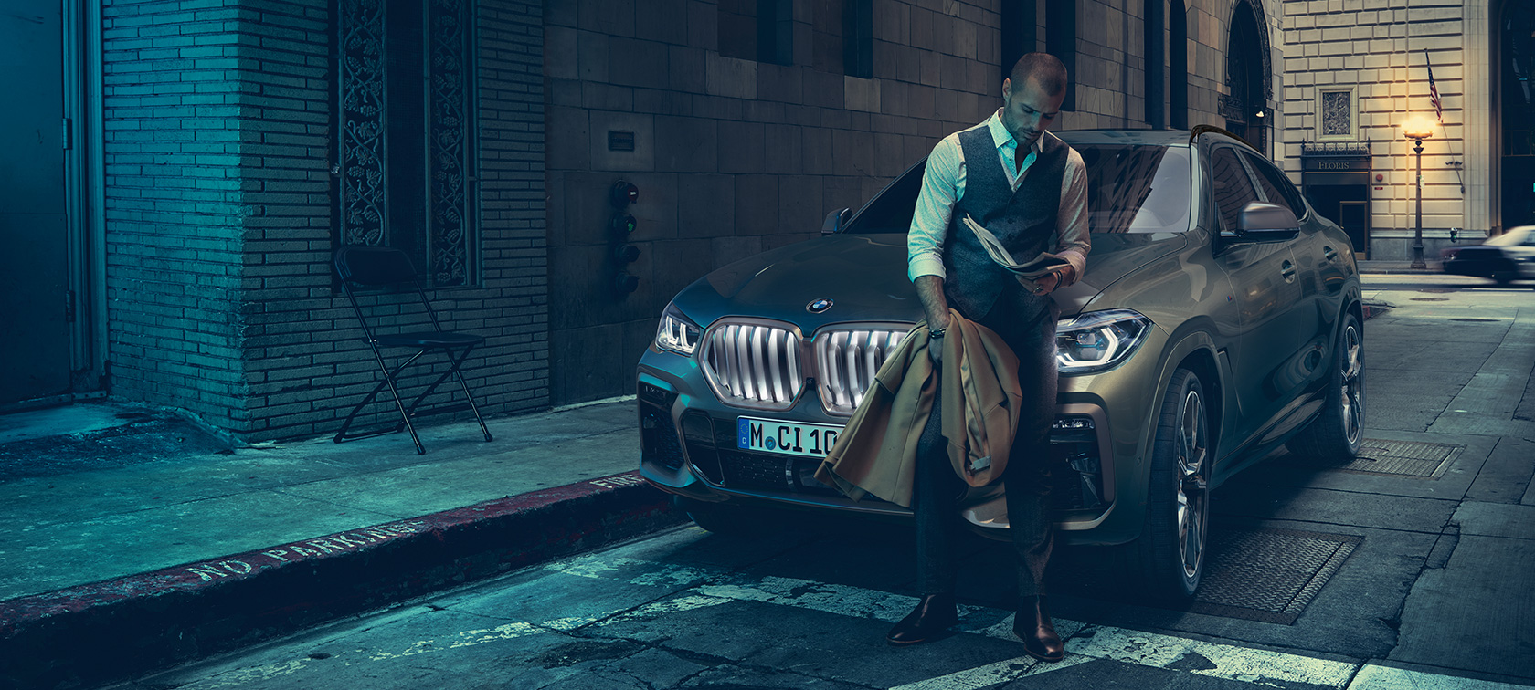 Čovjek naslonjen na BMW X6 Čovjek naslonjen na BMW X6 u bočnom prikazu ispred urbanog okruženja.