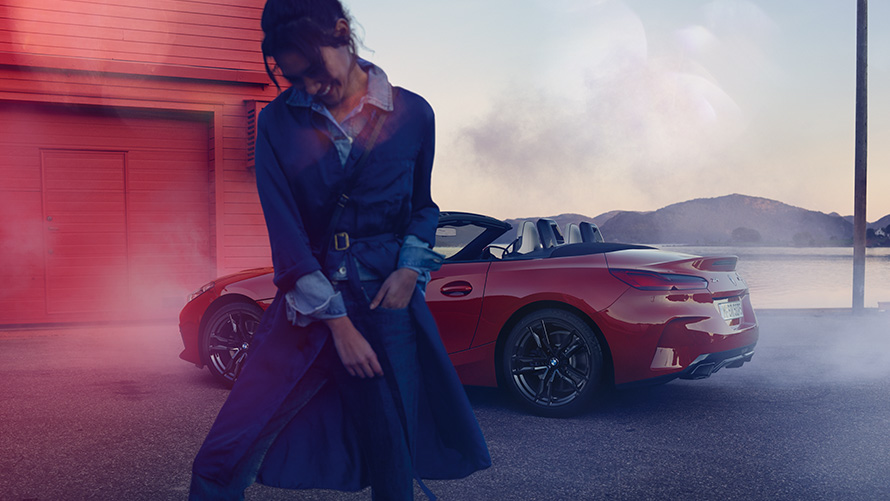 BMW Z4 M40i Roadster G29 sa otvorenim mekanim krovom BMW Z4 M40i Roadster G29 tročetvrtinski pogled straga sa otvorenim mekanim krovom i ženskom osobom u pozadini