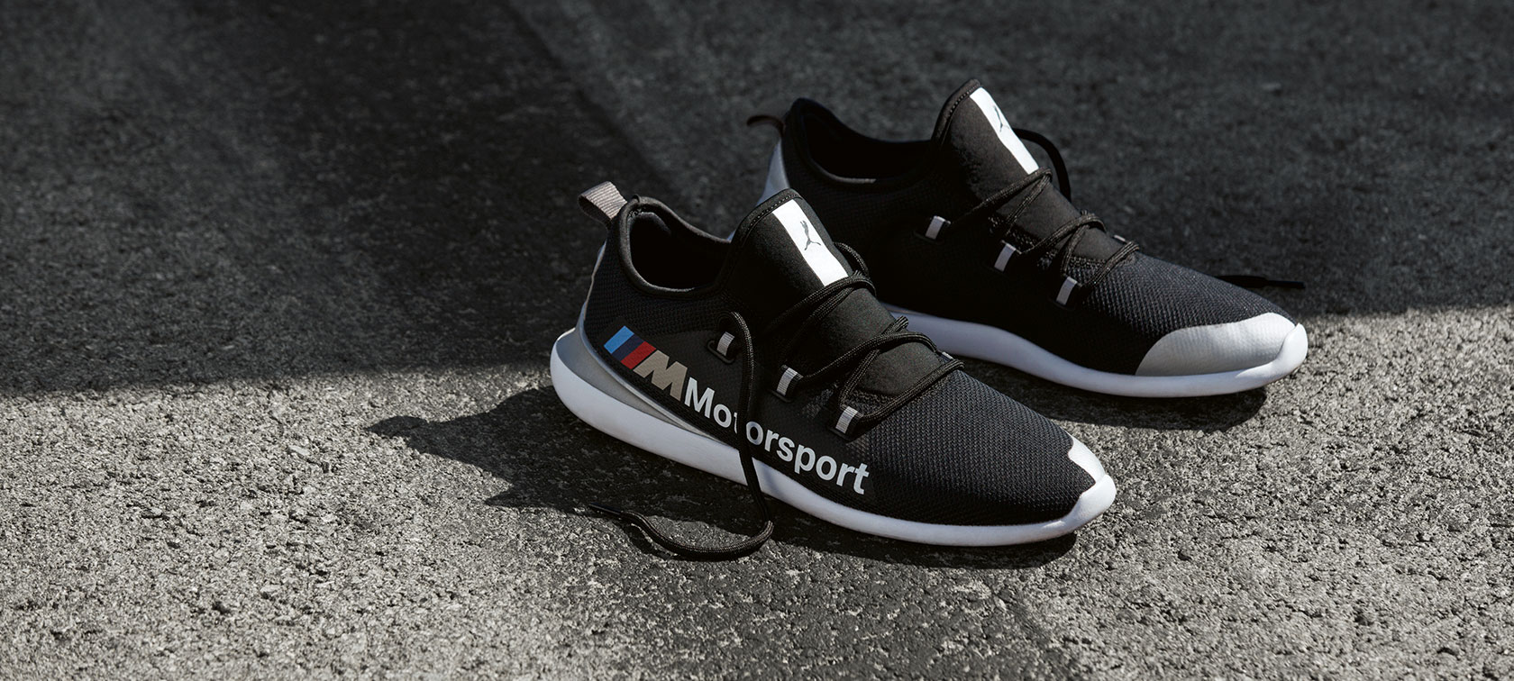 BMW M Motorsport PUMA EVO CAT cipele. Par BMW M Motorsport PUMA EVO CAT cipela iz BMW M Motorsport kolekcije na površini asfaltirane trkaće staze.