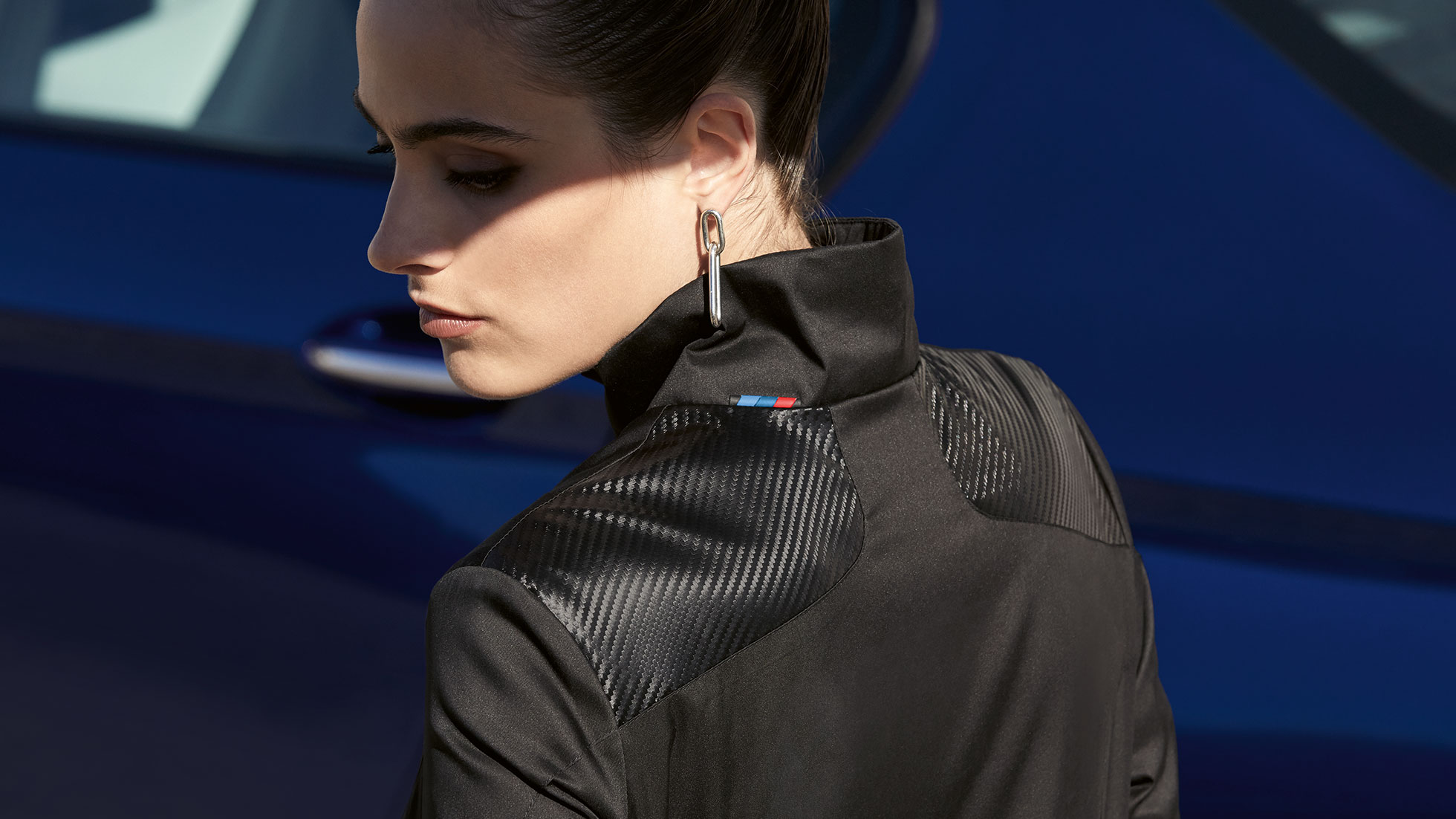 BMW m jakna, ženska. Žena je prikazana kako nosi žensku BMW M jaknu iz BMW M kolekcije. Detalji mješavine materijala.