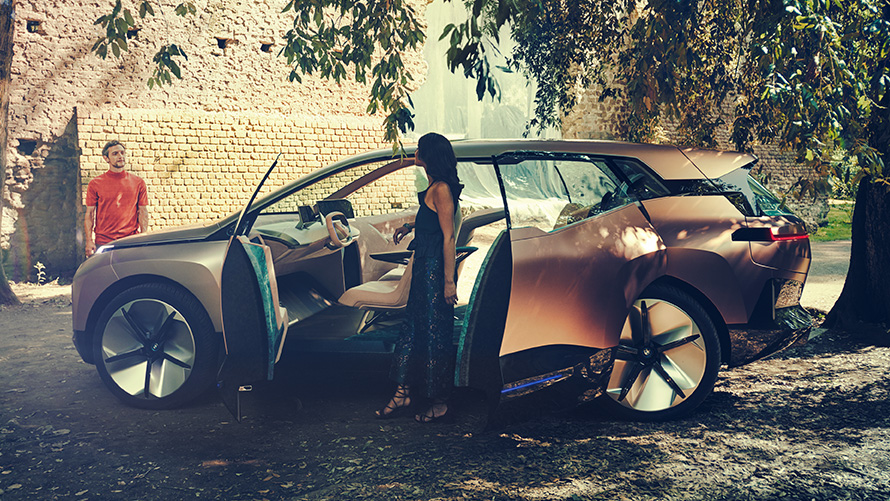 Bočni prikaz BMW-a Vision iNEXT Bočni prikaz BMW-a Vision iNEXT sa ženom na otvorenim vratima i muškarcem u pozadini
