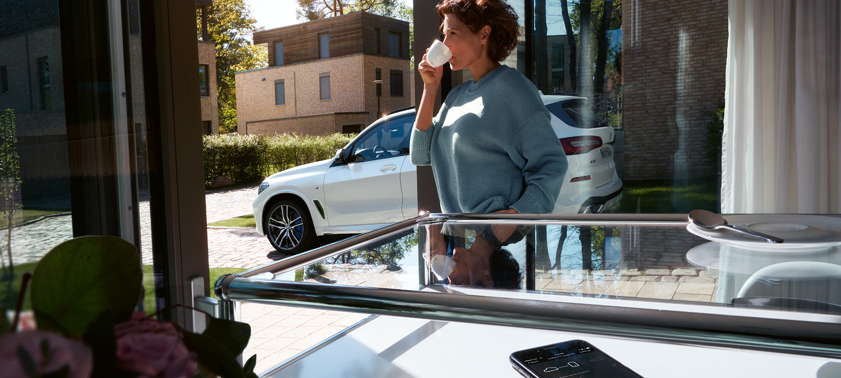 BMW Remote Software Upgrade Ženska osoba pije iz šalice sa BMW Remote Software Upgrade ažurira softver svog BMW X5