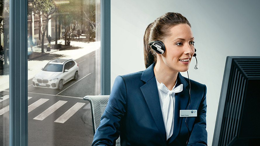 Concierge Services (usluge) Concierge Services: Zaposlenik BMW-a sjedi za svojim stolom i nosi slušalice