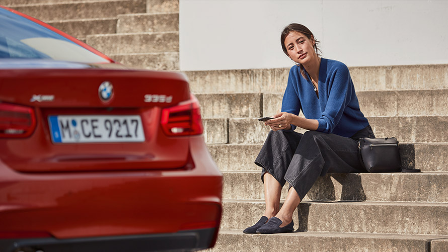 Pomoć i usluga u slučaju kvara Žena sjedi ispred svog BMW-a i koristi Pomoć i uslugu u slučaju kvara