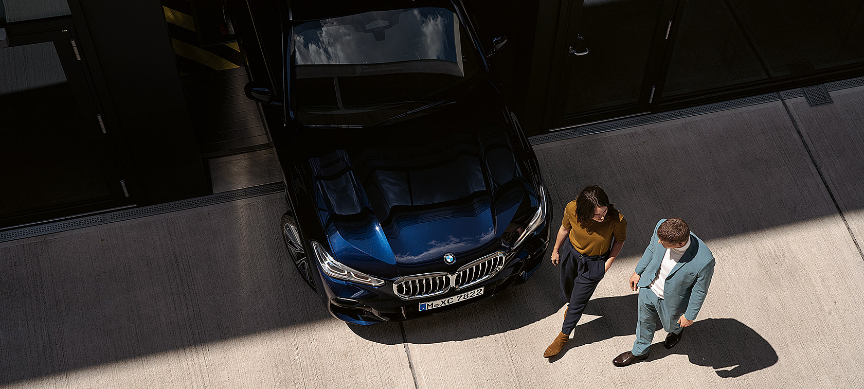 Žena i muškarac prolaze pored prednjeg dijela BMW-a Žena i muškarac prolaze pored prednjeg dijela BMW-a iz ptičje perspektive