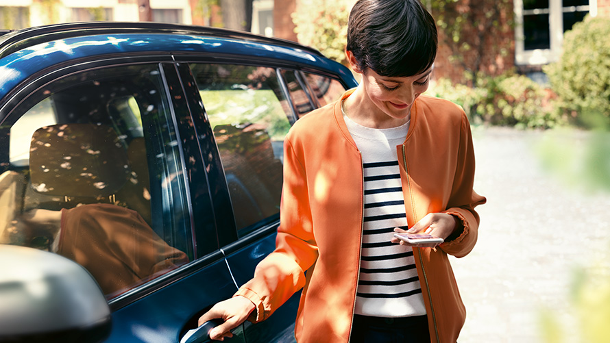 BMW Teleservices Žena sa pametnim telefonom stoji na vratima svog BMW-a