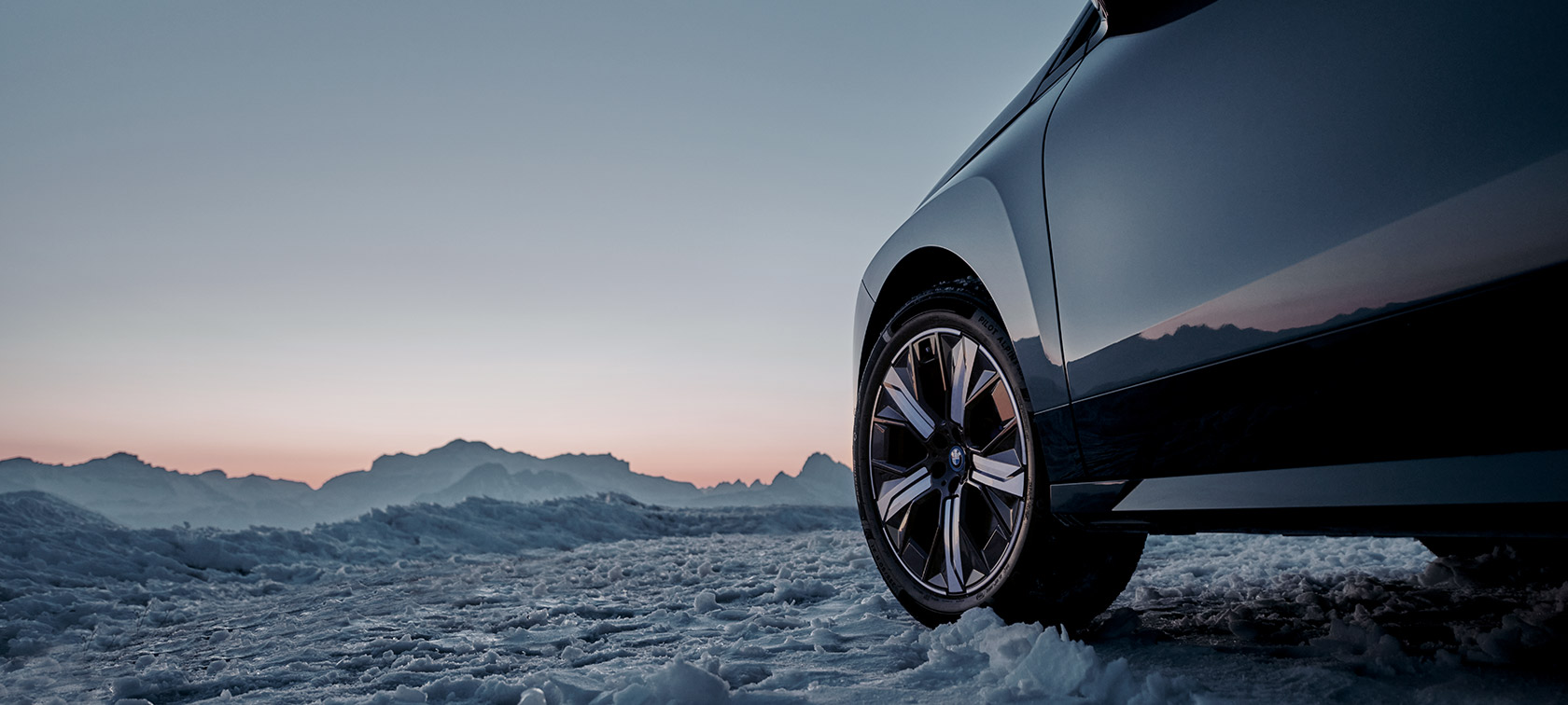 Originalni BMW kotači na BMW-u iX (I20) na snijegu ispred planina Originalni BMW kotači na BMW-u iX (I20) na snijegu ispred planina