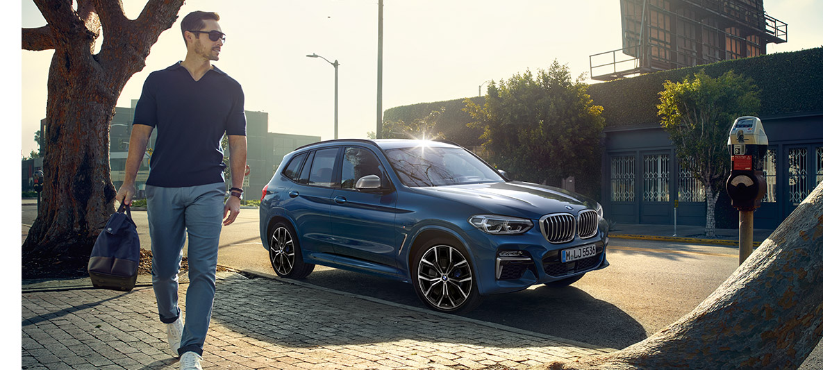 Muškarac sa sunčanim naočalima ispred plavog BMW-a Muškarac sa sunčanim naočalima ispred plavog BMW-a