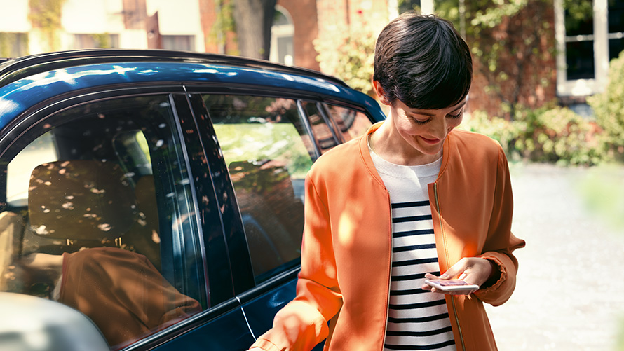 BMW ljetna ponuda BMW Teleservices BMW ljetna ponuda BMW Teleservices: žena stoji ispred BMW-a i koristi pametni telefon